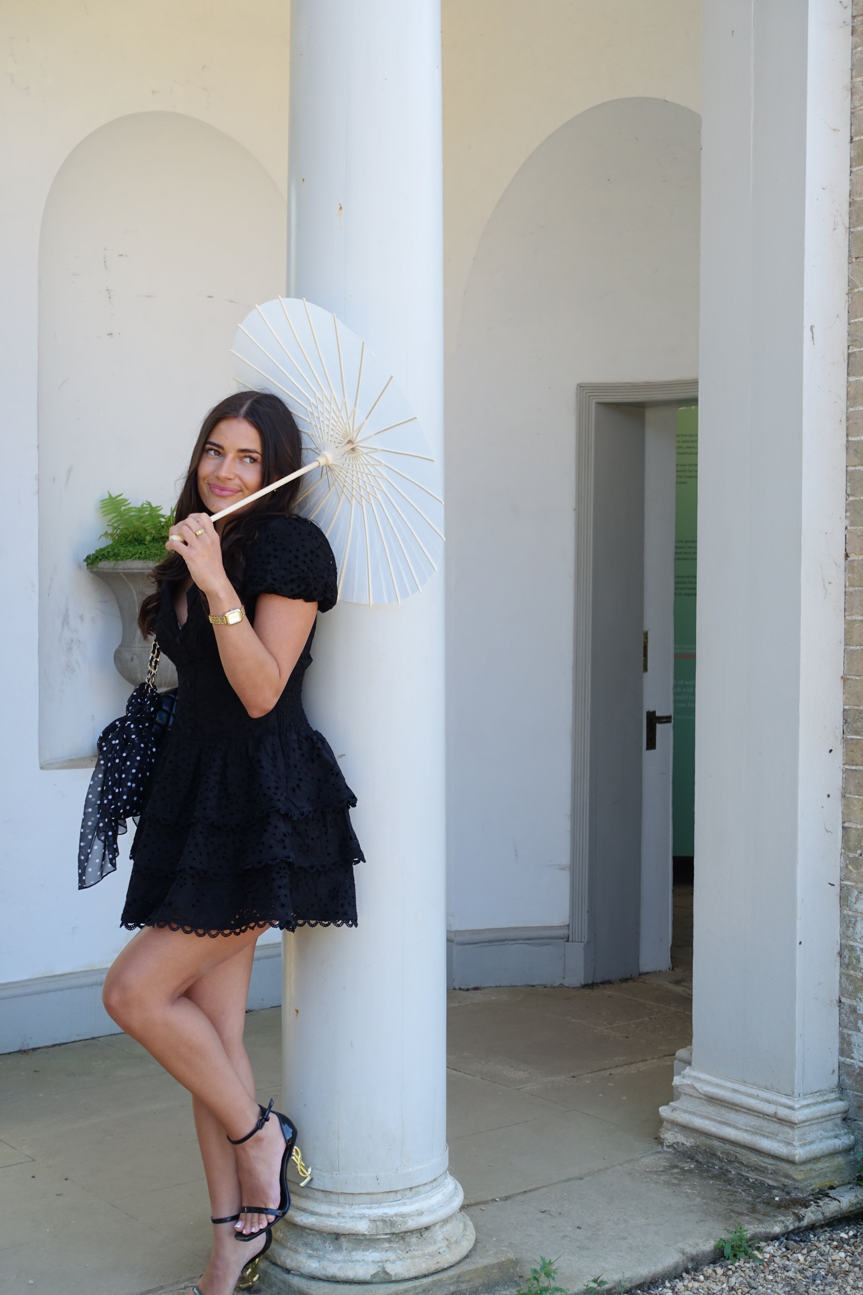 Woman in a black dress holding a white parasol against a neutral background