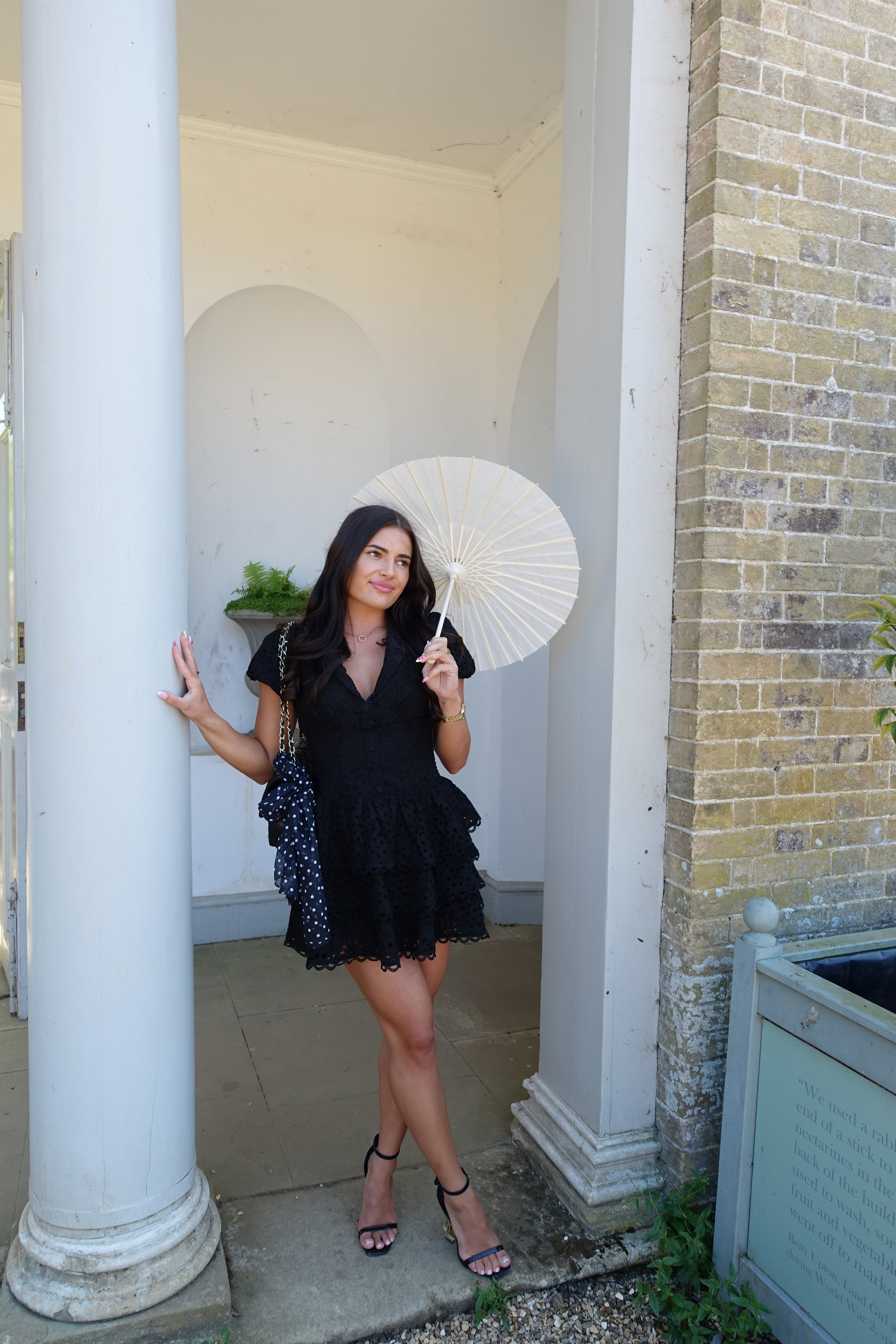 Woman in a black dress standing on a staircase with a white column in the foreground.