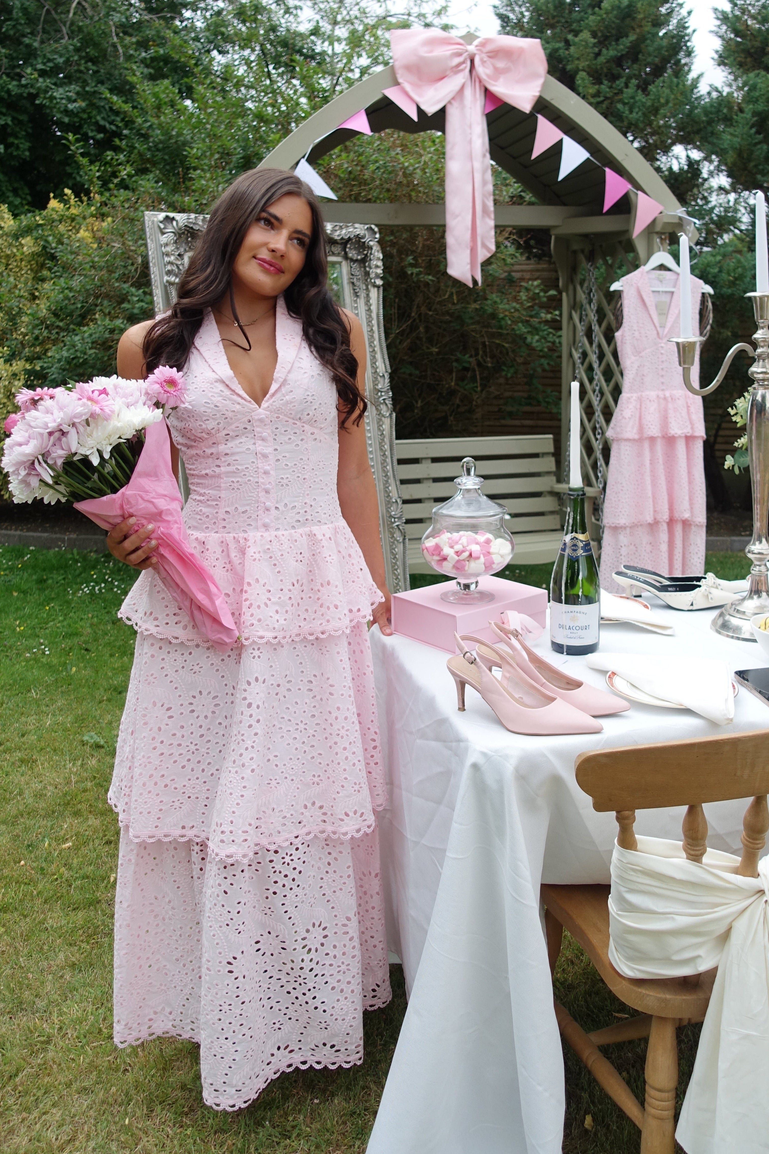 Woman in a pink dress standing in front of a decorated outdoor setting with chairs and bunting.